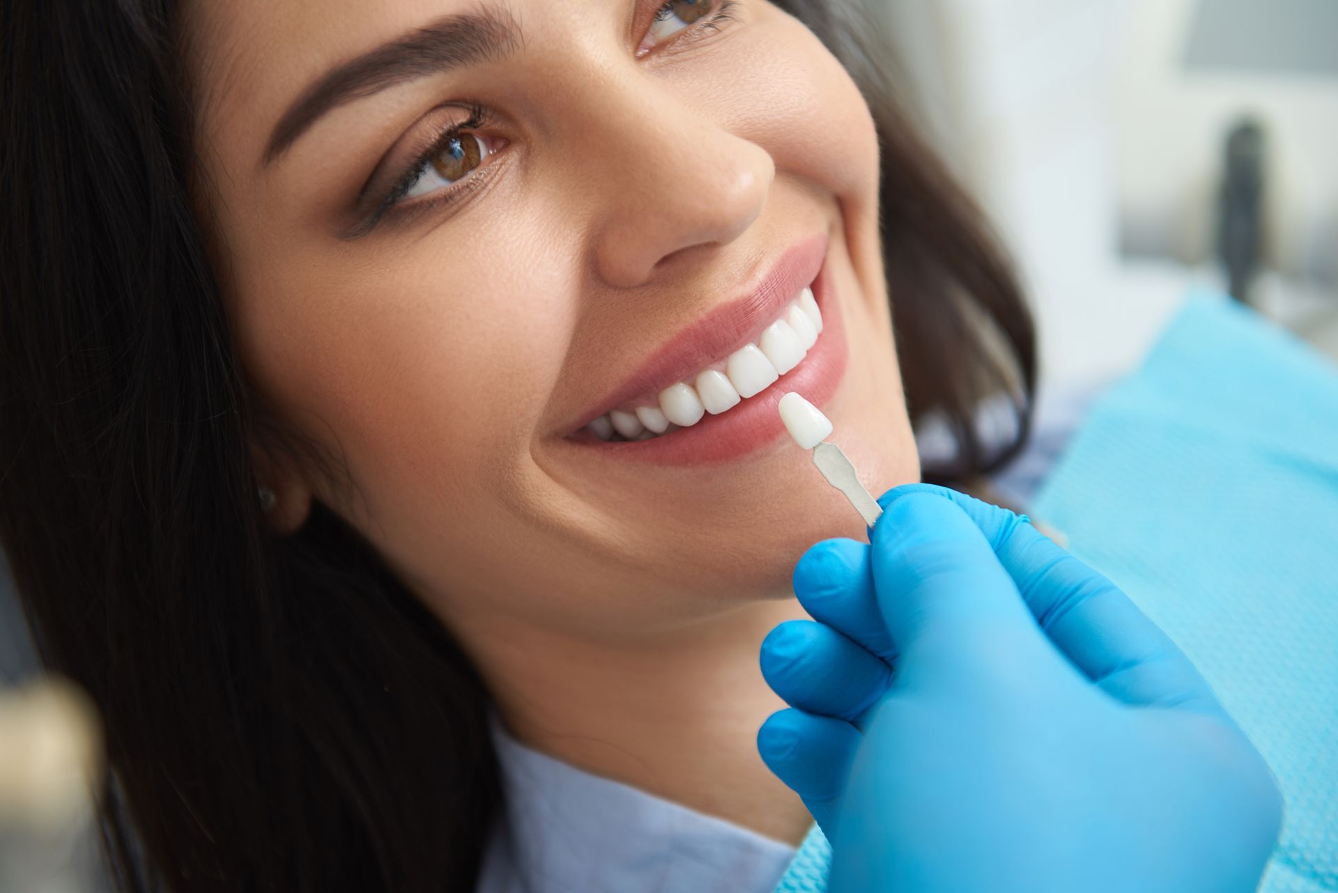 A dentist applies a tooth-whitening gel with a blue-gloved hand as a smiling patient reclines.