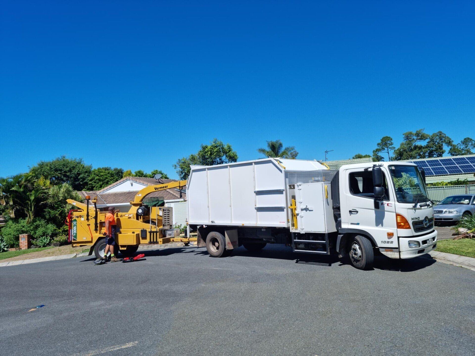 A white truck is parked on the side of the road next to a tree chipper.