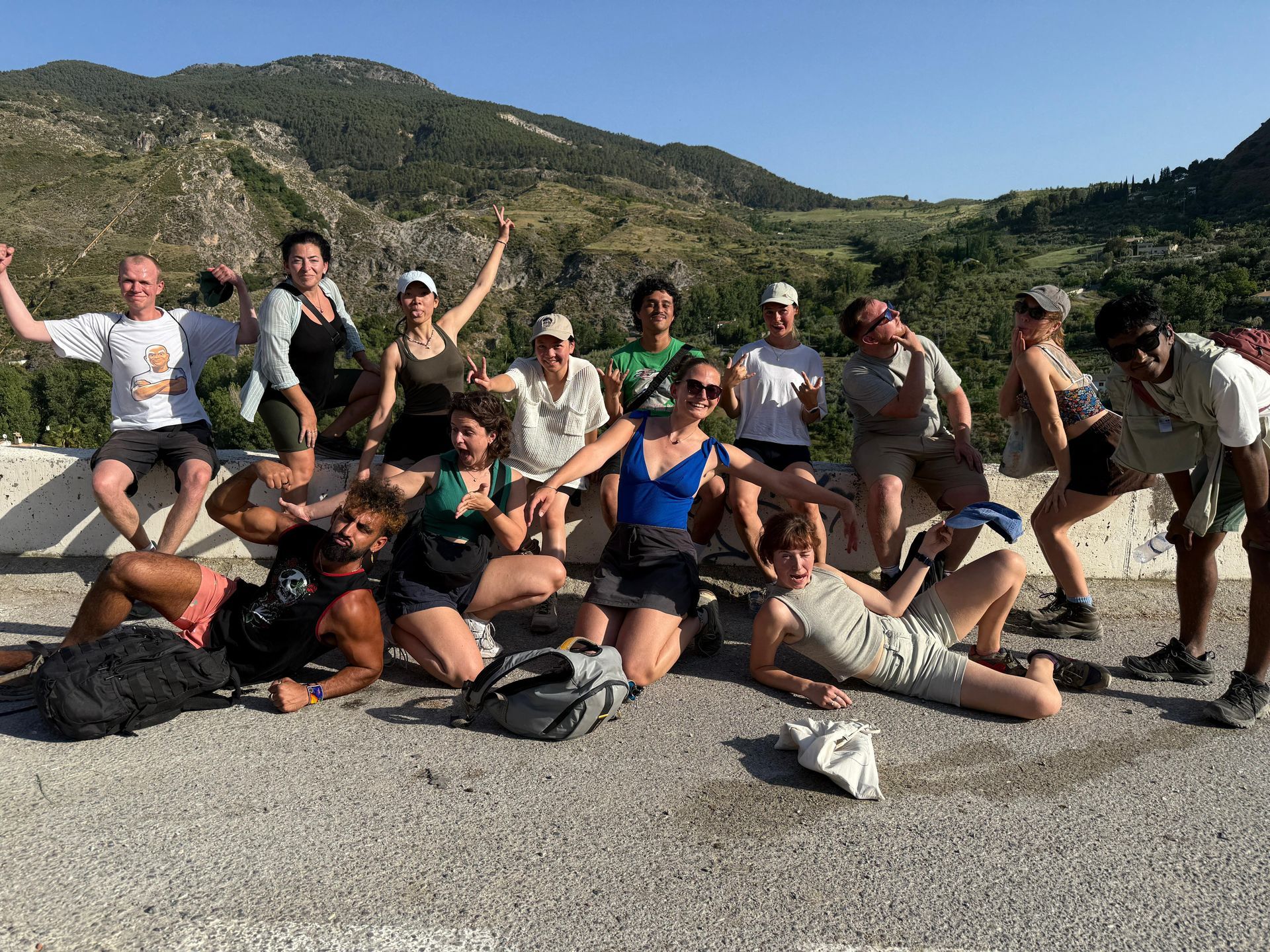 Group of hikers posing happily on a rocky mountain trail with backpacks, green hills in the background