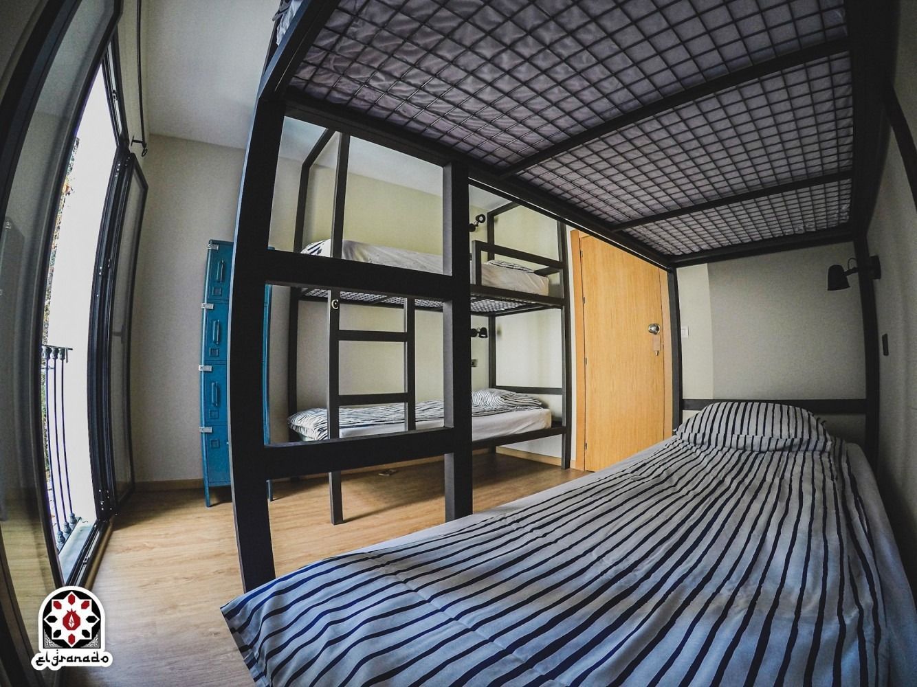 Bright modern bedroom with green accent wall, black doors, bed, sofa, and small table near tall windows