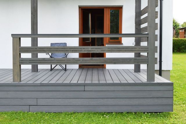 A wooden deck with a chair on it in front of a white house.