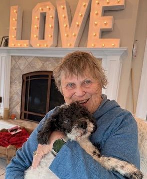 Woman sitting on a couch with a brown dog standing beside her, both looking toward the camera.