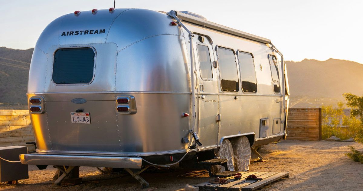 A silver airstream trailer is parked in a dirt lot.
