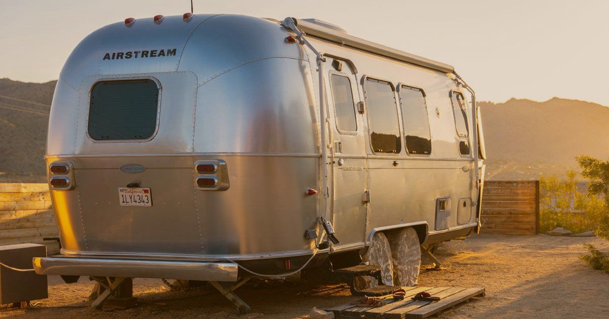 A silver airstream trailer is parked in a dirt lot.