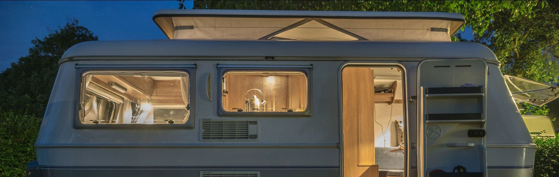 A camper is parked in a parking lot at night with the door open.