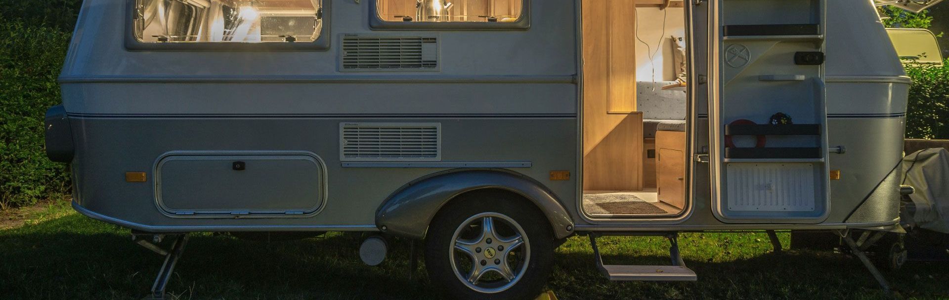 A small trailer is parked in the grass with the door open.