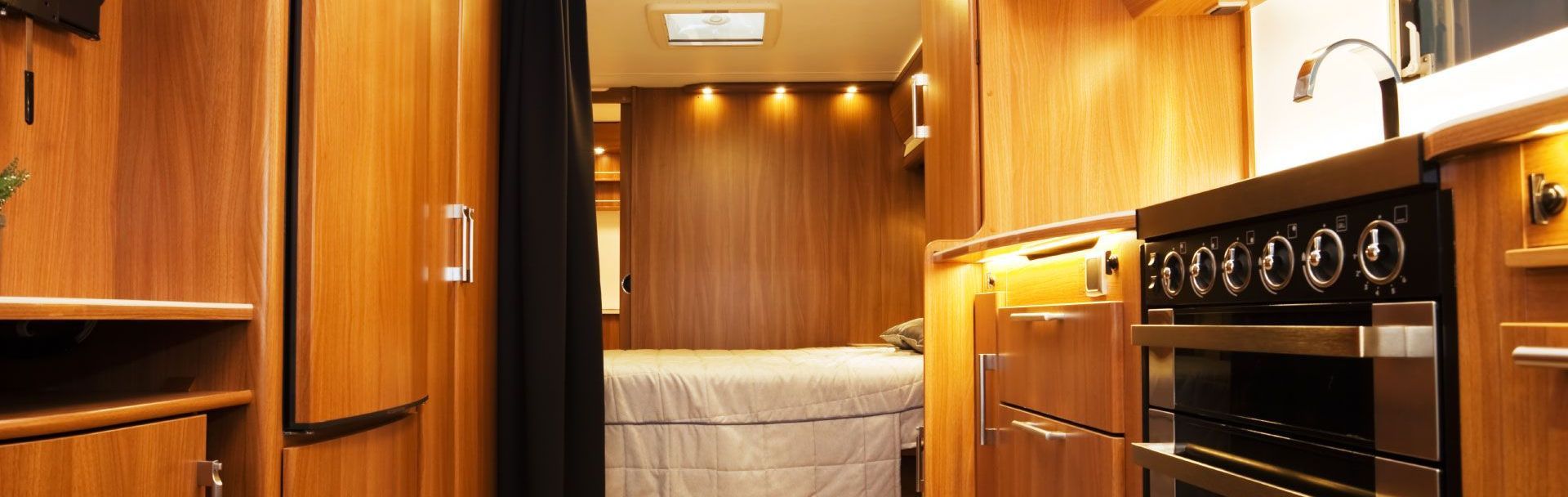 A kitchen in a camper with wooden cabinets and stainless steel appliances.