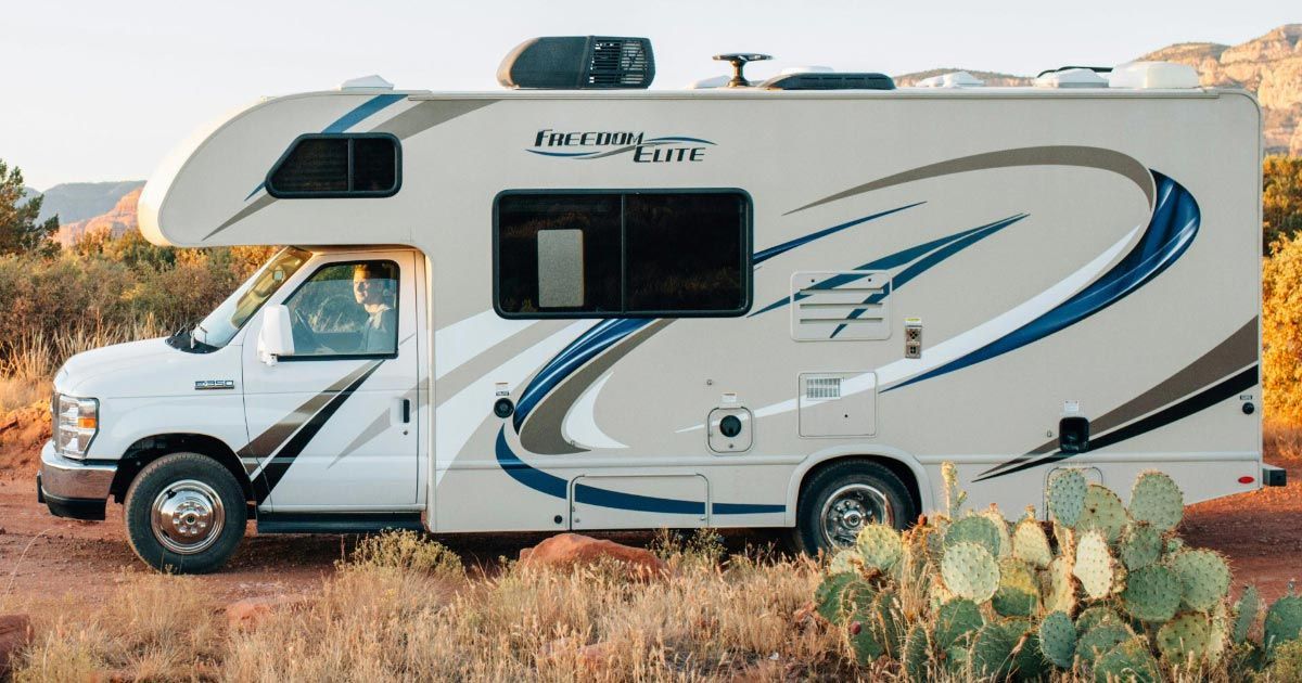 A white rv is parked in a field next to a cactus.