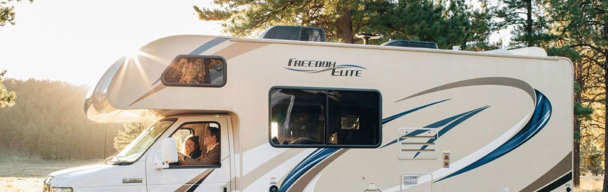 A white rv is parked next to a tree in a field.