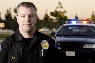 A police officer is posing for a picture in front of a police car.