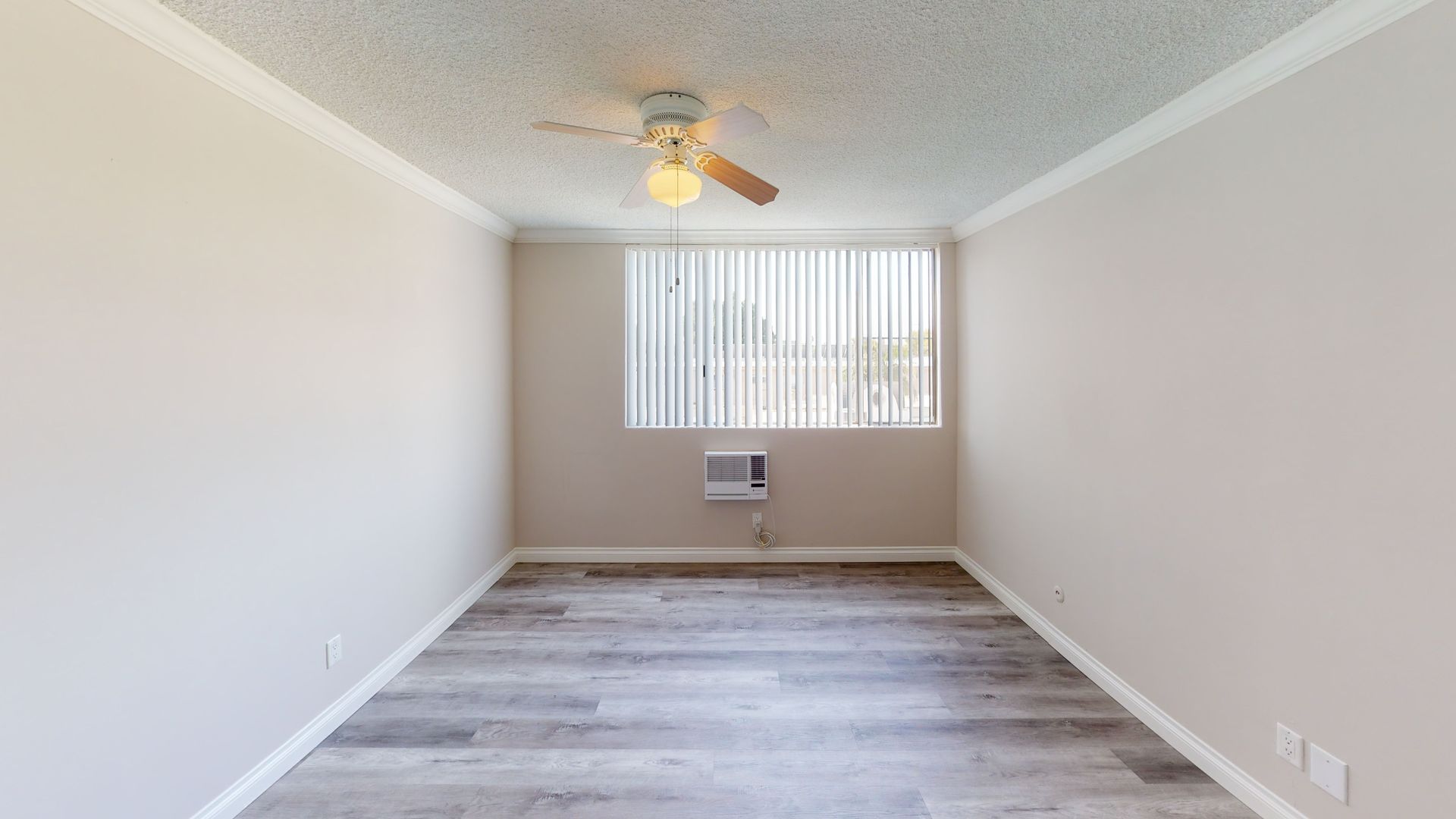 Empty room with wooden floors, tan walls, window with blinds, and ceiling fan.