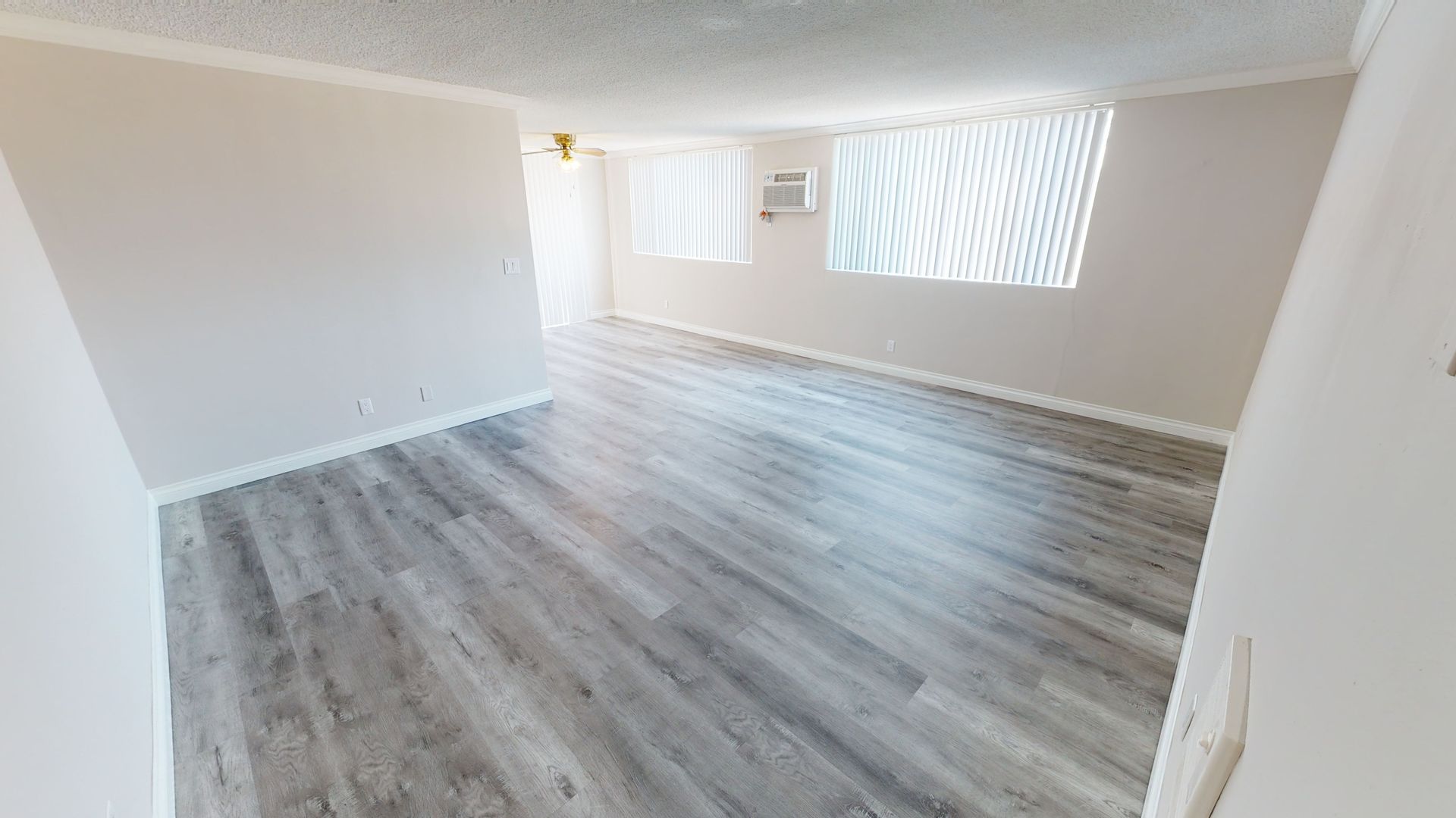 Empty room with wood-look flooring and white walls. Two windows with blinds, air conditioner.