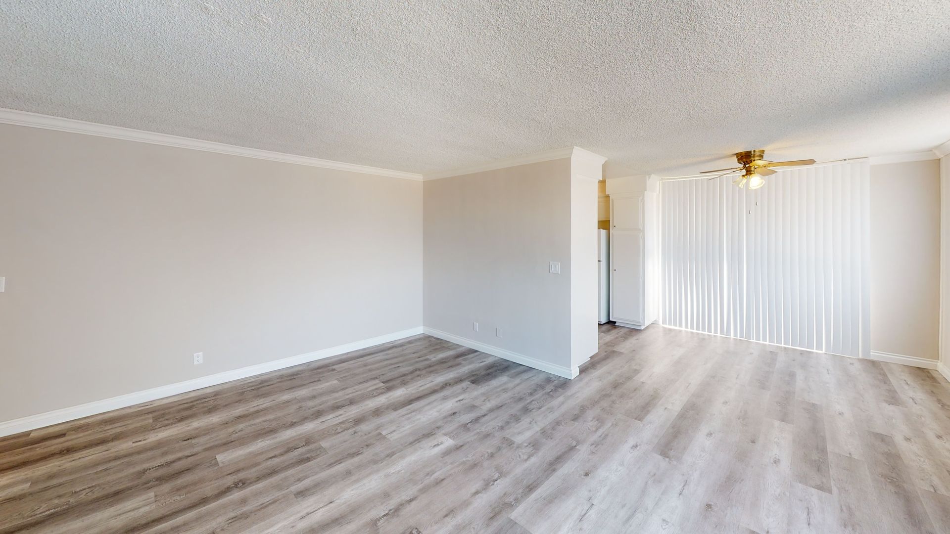 Empty living room with wood-look flooring, white walls, and vertical blinds. Ceiling fan present.