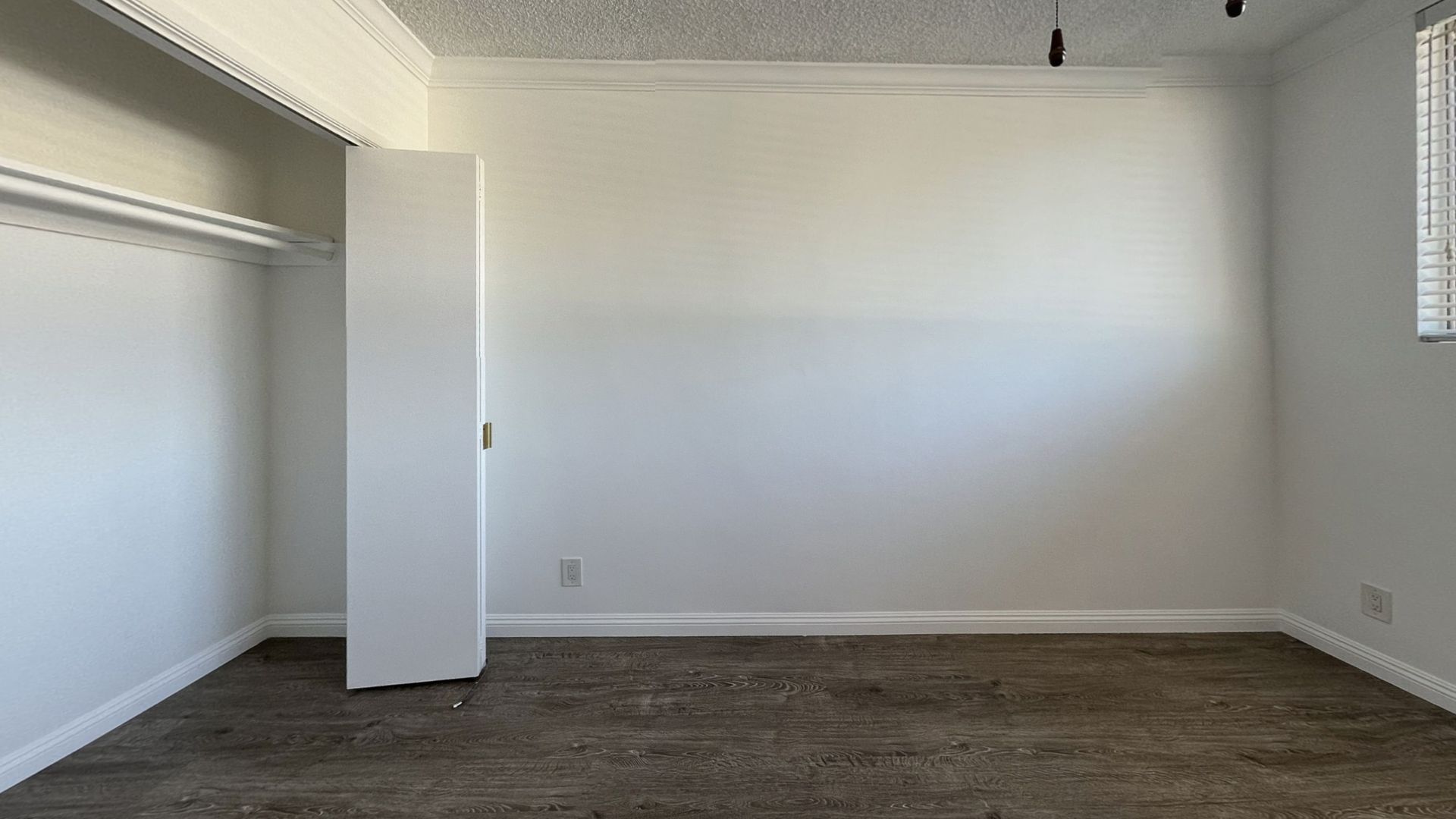 Empty room with white walls, closet door ajar, dark carpet, and a window with blinds.