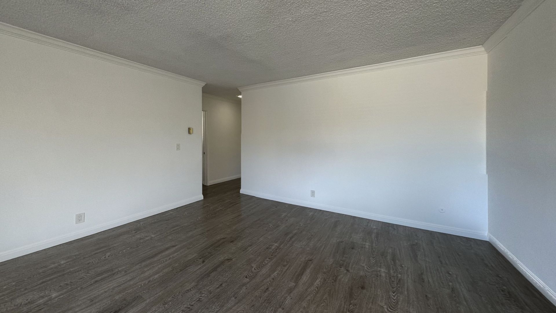 Empty room with white walls, textured ceiling, and dark wood-look flooring.