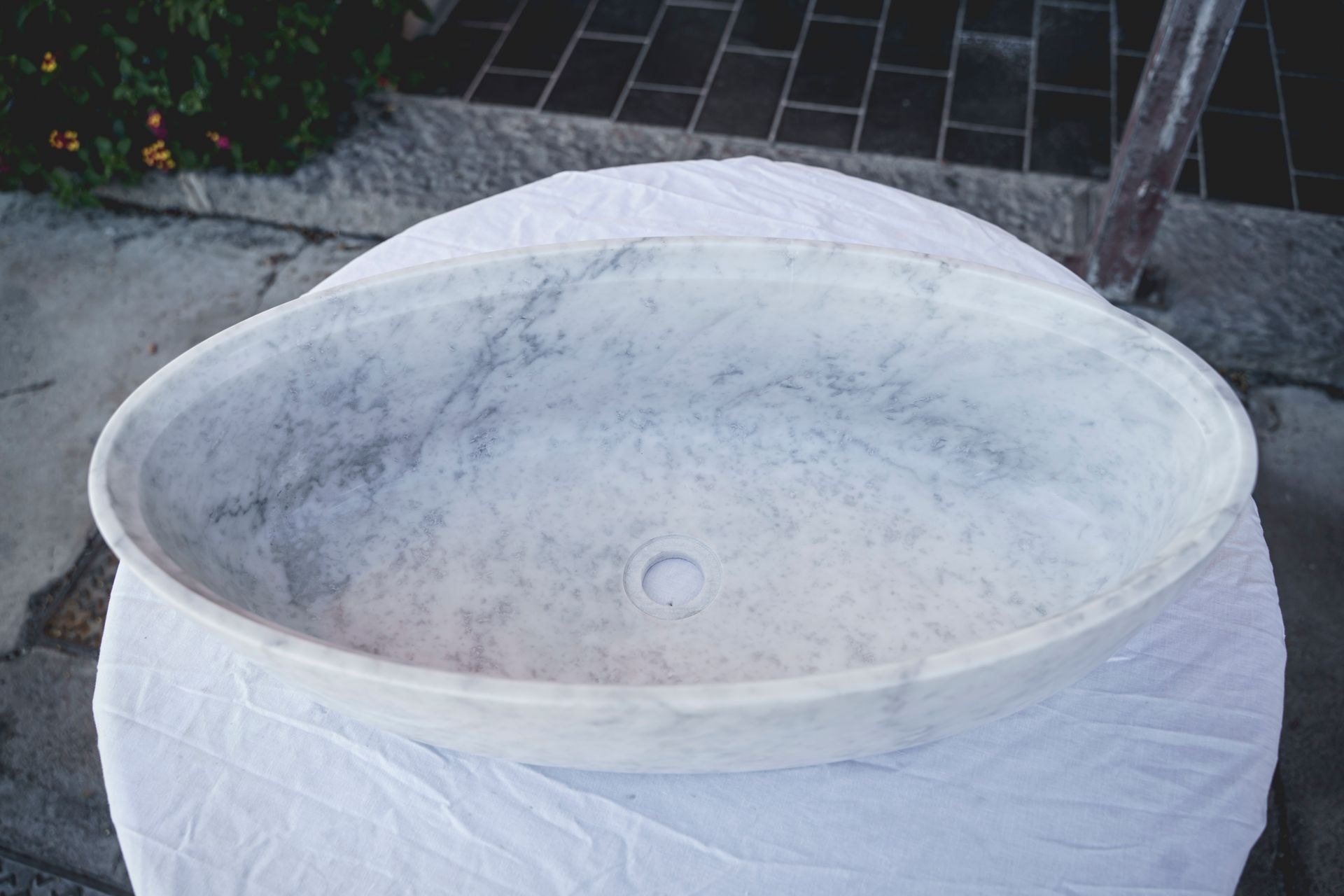 Lavandino ovale in marmo su tessuto bianco, con fondo decorato in grigio scuro.