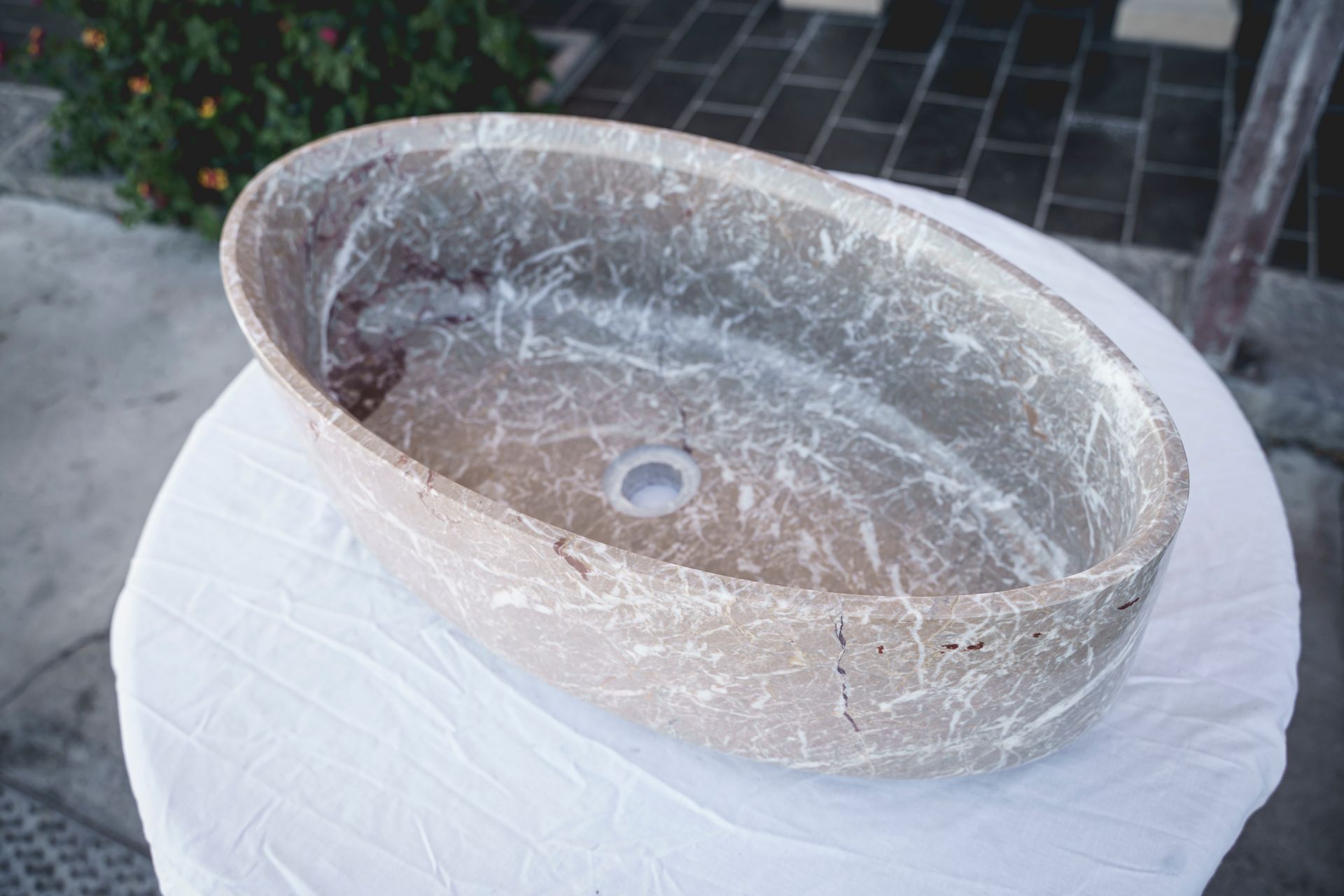 Lavandino ovale con motivo marmoreo su un tavolo ricoperto di stoffa bianca.