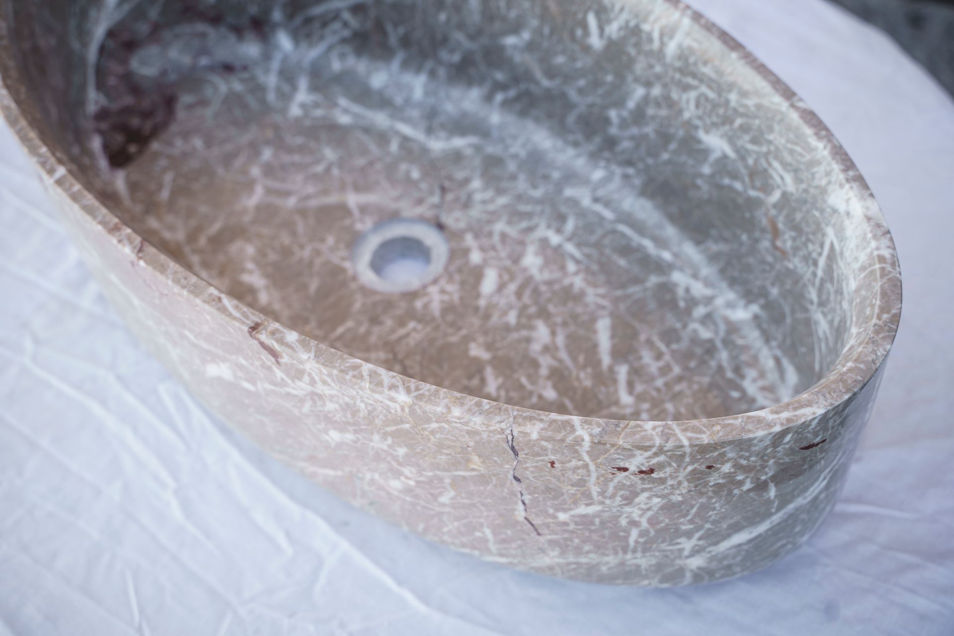 Lavandino da bagno in pietra di forma ovale con motivo marmorizzato, visto dall'alto.