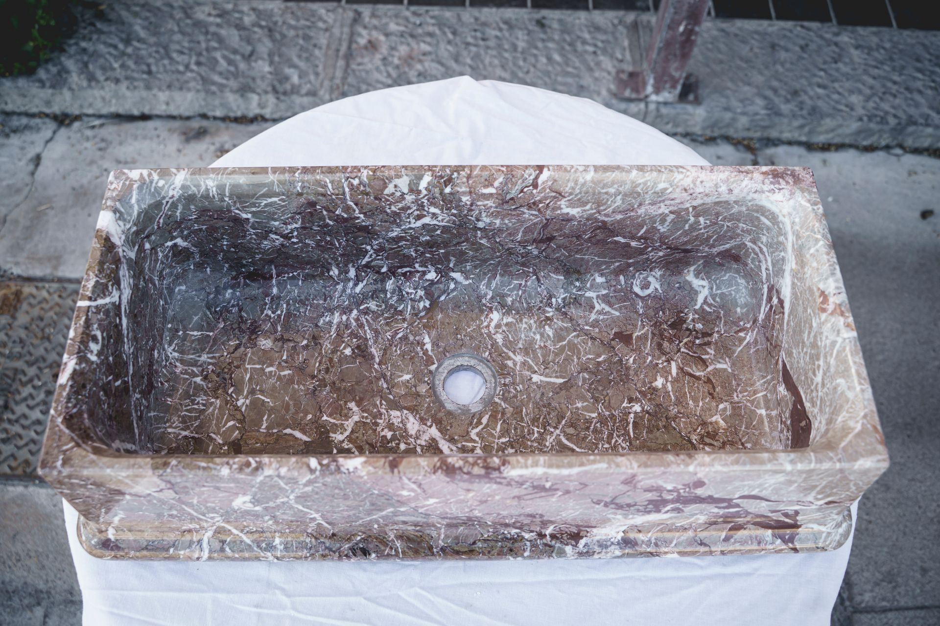 Lavandino da bagno rettangolare in pietra con venature marroni e bianche, appoggiato su un tavolo rivestito di bianco.