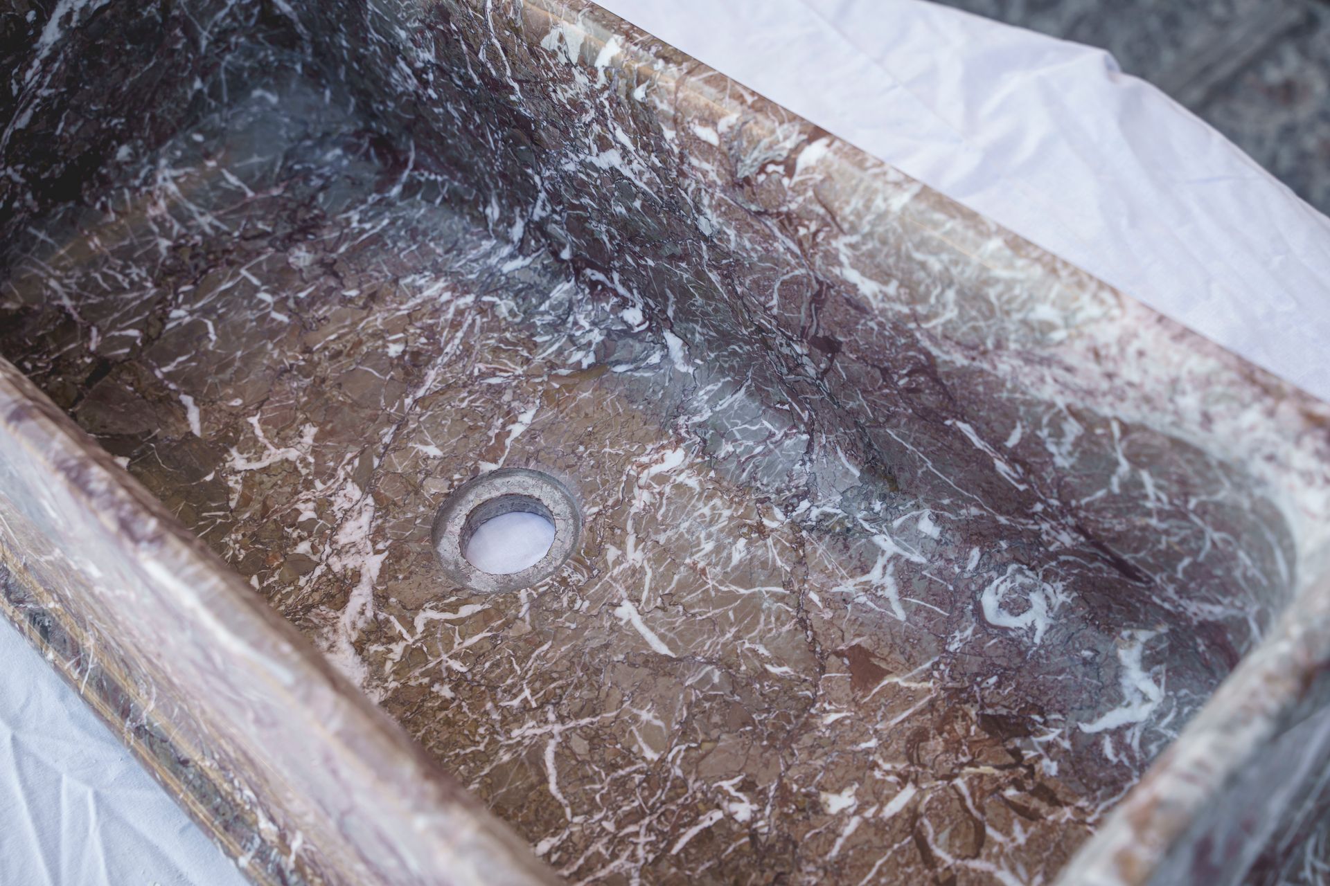 Lavandino da bagno in marmo con foro di scarico, con venature marrone chiaro e scuro.