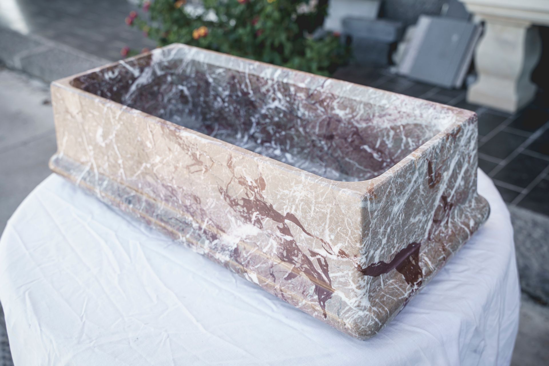 Lavabo rettangolare in marmo con venature marroni e bianche, appoggiato su una tovaglia bianca.