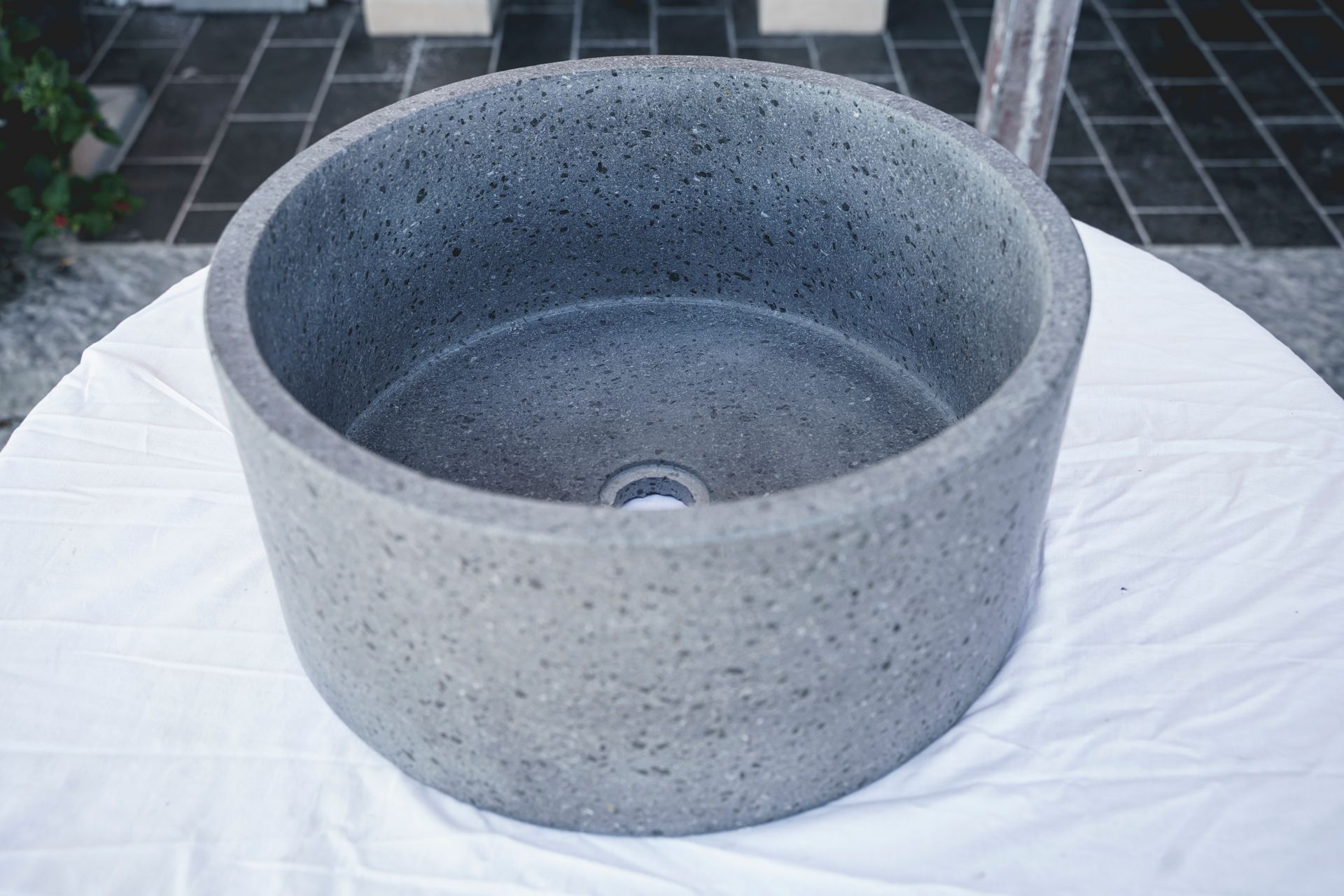 Vasca cilindrica in cemento grigio con scarico, su superficie bianca.