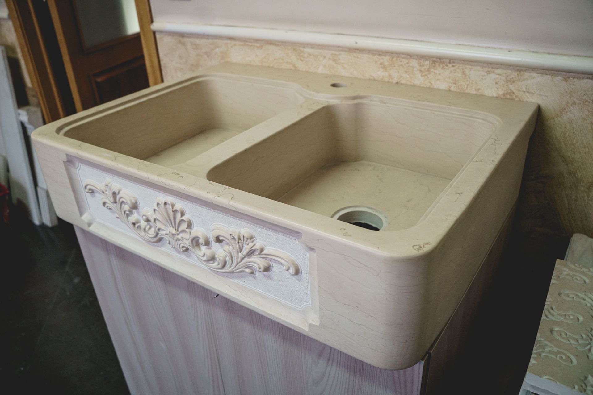 Lavandino beige a doppia vasca con pannello decorativo intagliato su un mobile di colore chiaro.