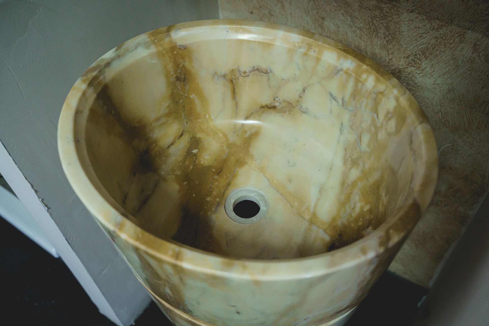 Lavandino rotondo con piedistallo in pietra venata color marrone chiaro e marrone, con foro di scarico.