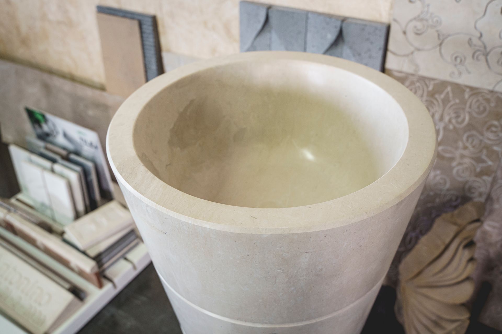 Lavandino con piedistallo in pietra bianca e vasca rotonda, ambientato in uno showroom.