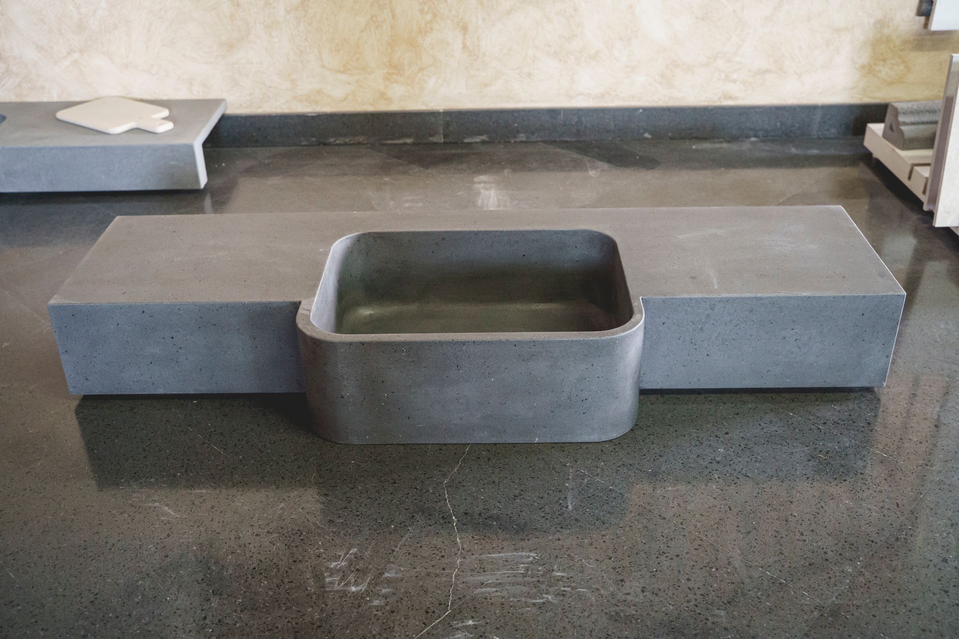 Lavello rettangolare in cemento grigio su un piano di lavoro scuro con parete di sfondo di colore più chiaro.