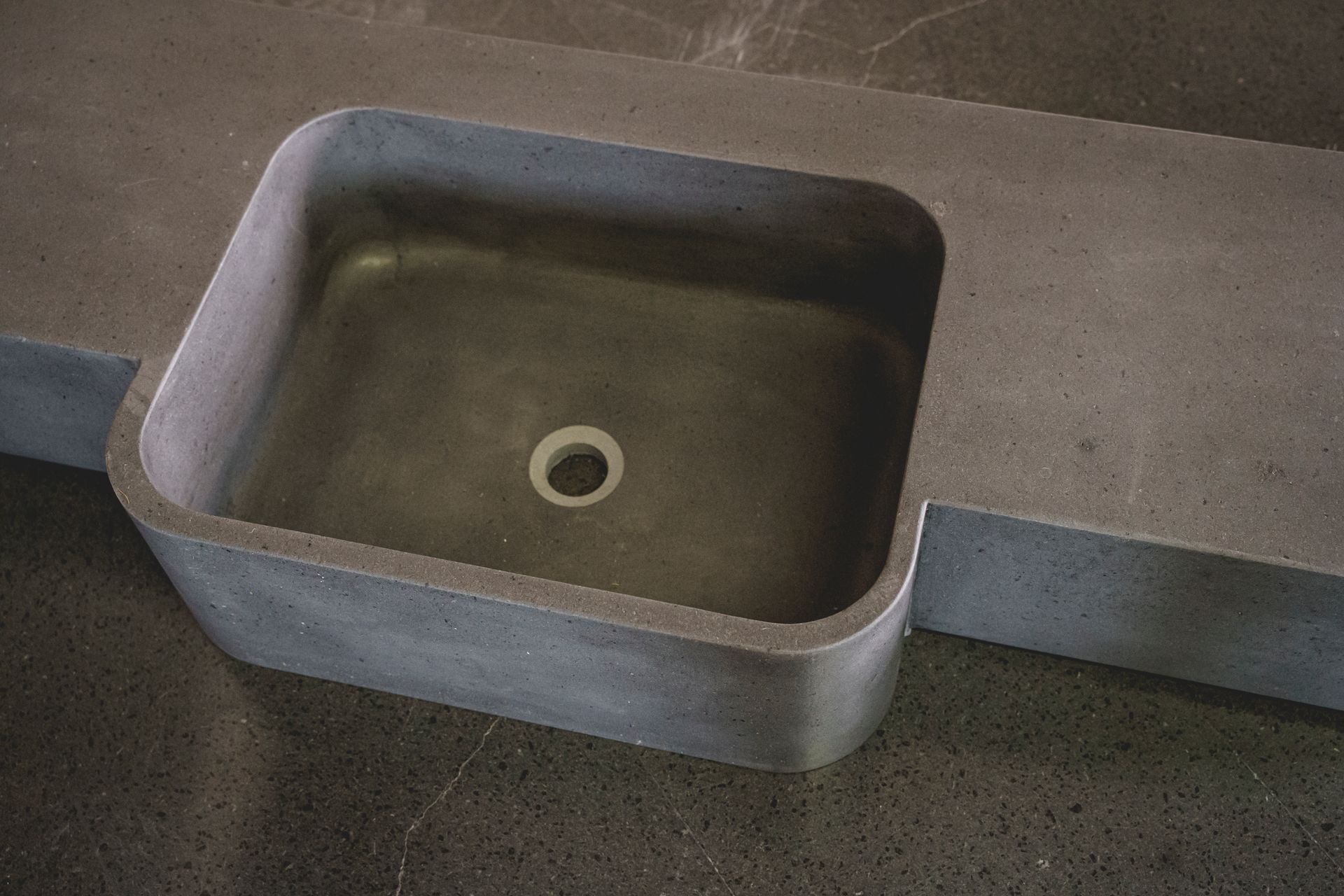 Piano di lavoro in cemento con lavello quadrato integrato. Grigio con interno liscio e angoli arrotondati.