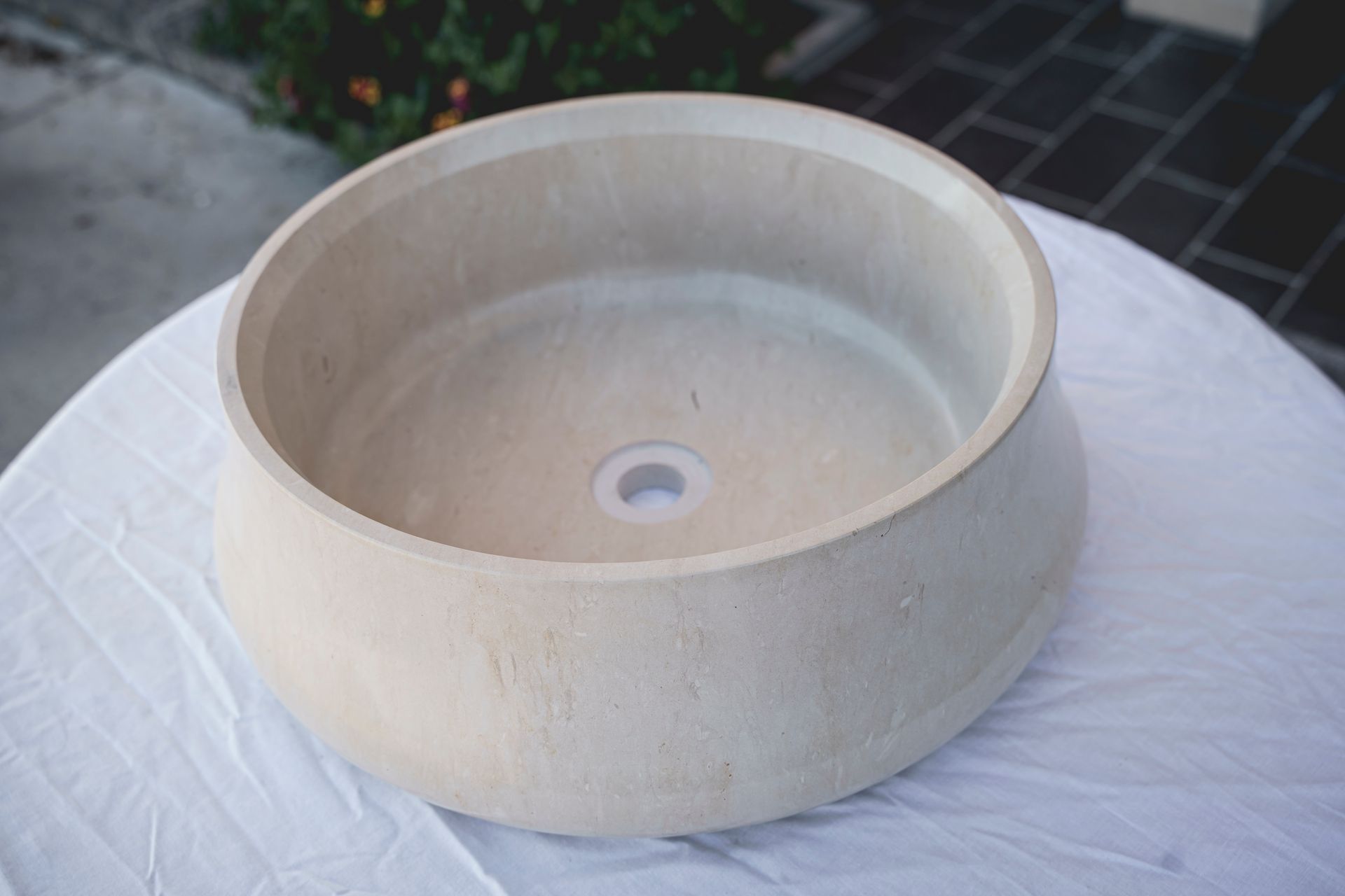 Lavandino in pietra beige con scarico bianco su tovaglia bianca.