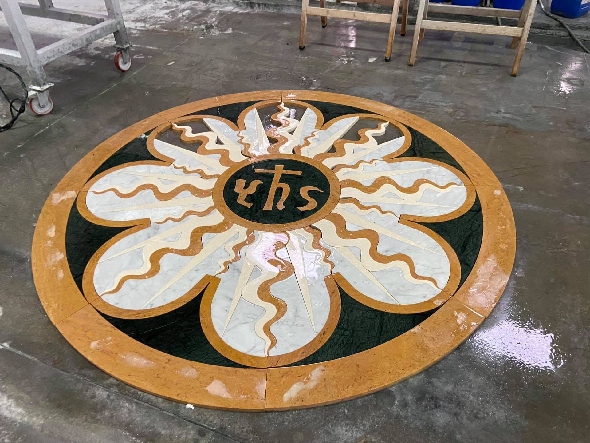 Pavimento circolare in pietra intarsiata con simboli floreali e religiosi. Colori giallo, nero, bianco e marrone.
