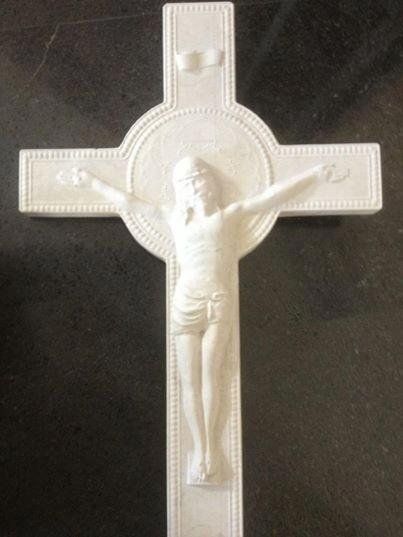 Crocifisso bianco con figura di Gesù. Braccia tese, in rilievo, su sfondo scuro.