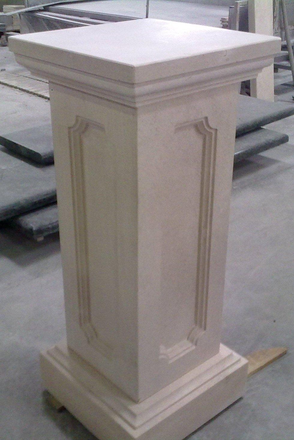 Piedistallo in pietra con parte superiore quadrata, pannelli decorativi sui lati e base quadrata.