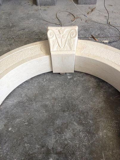 Segmento di arco in pietra scolpita con capitello decorativo, colore chiaro, su pavimento grigio.