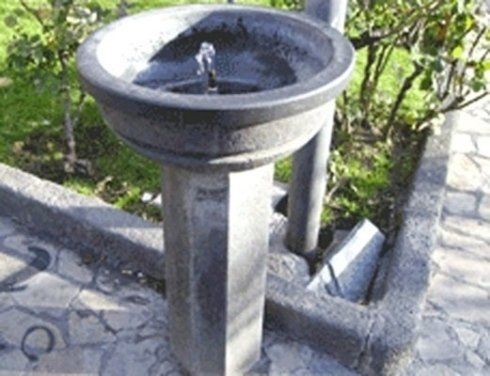 Fontana pubblica in pietra grigia in un parco, acqua che scorre.