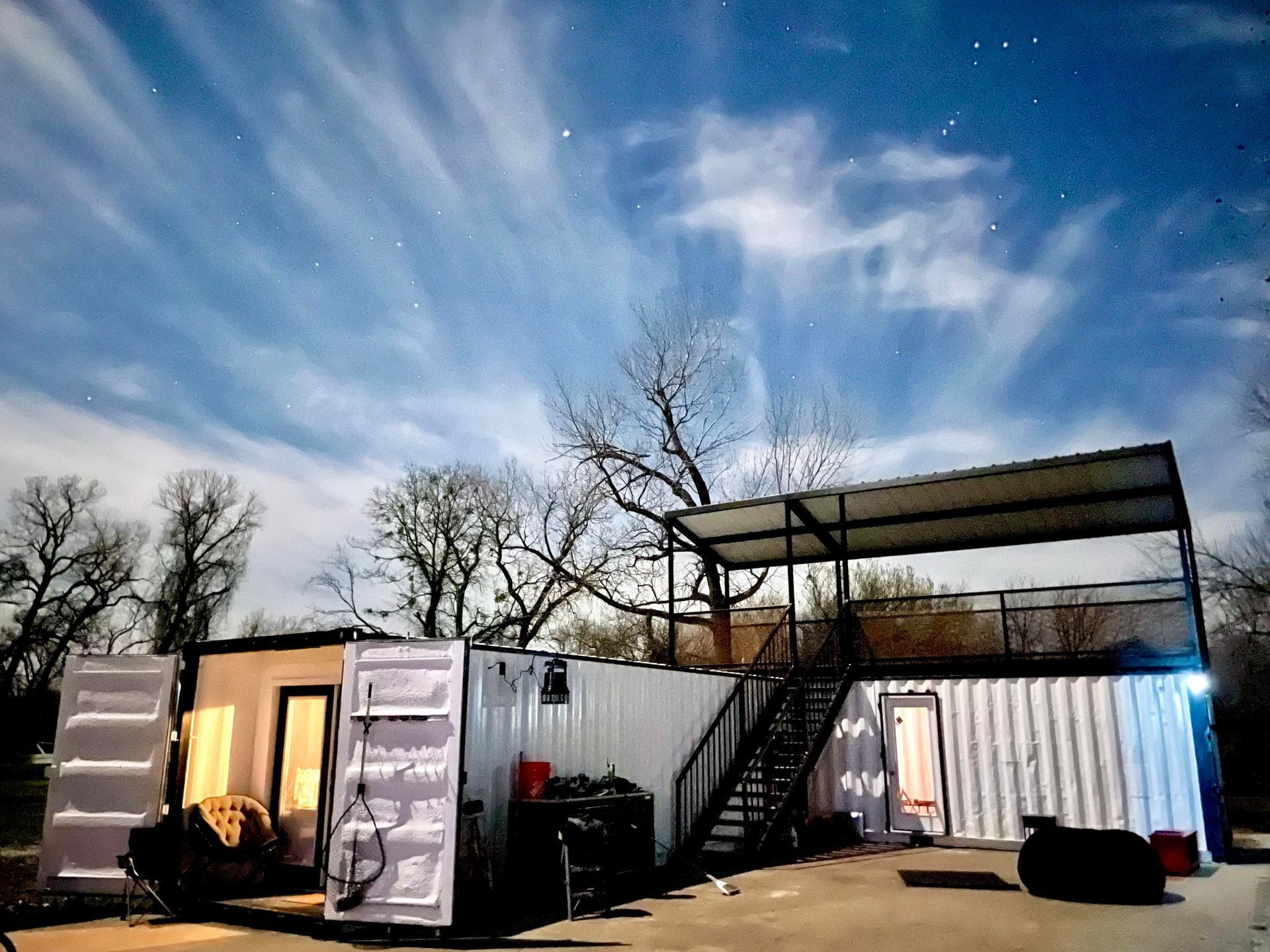 A couple of shipping containers are parked in front of a house at night.