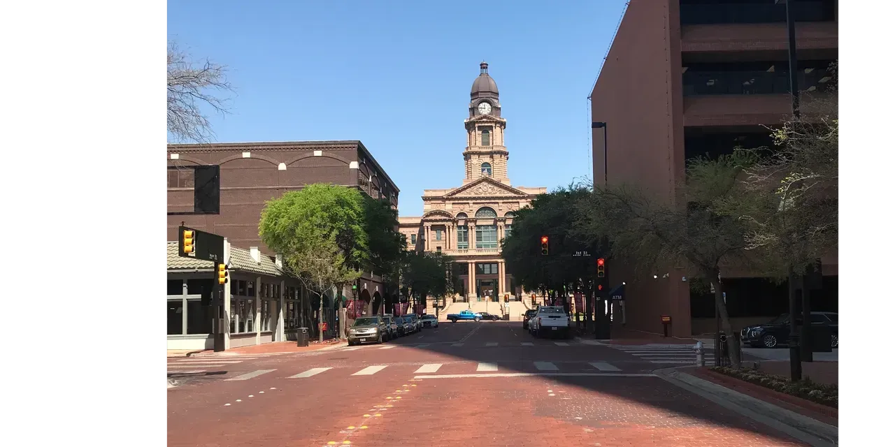Street view of a brick road leading to a tall building with a clock tower under a clear sky.