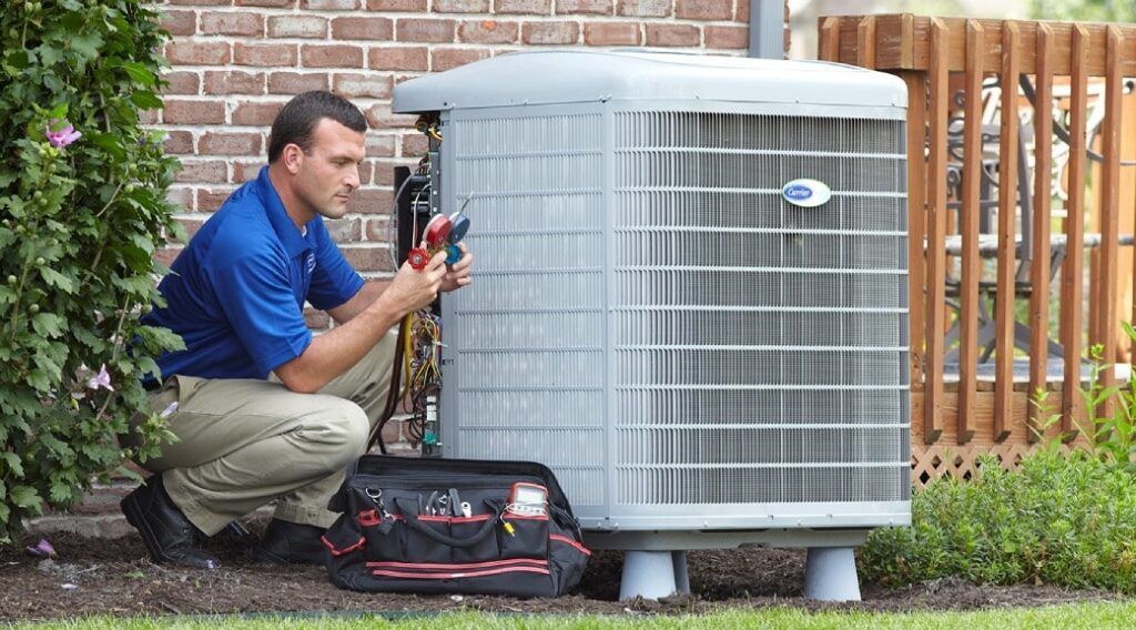 HVAC technician kneeling beside an air conditioning unit, using tools, outdoors.
