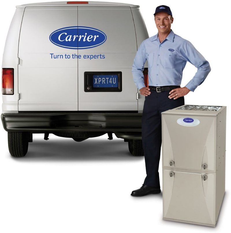 Carrier technician stands next to a van and furnace. He's smiling. Van is white.