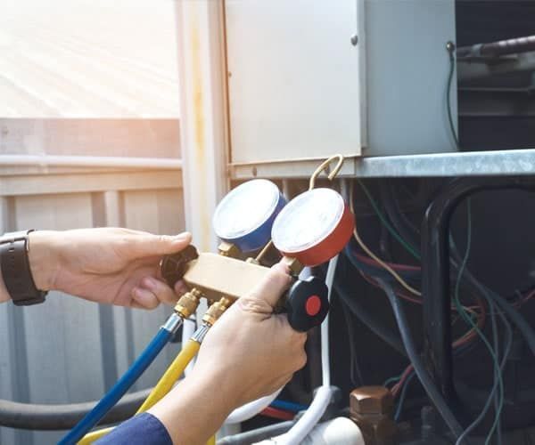 Person using gauges to service an air conditioning unit outdoors.