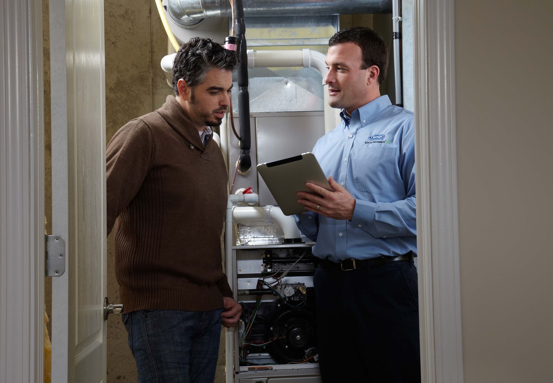 HVAC technician in blue shirt discusses thermostat with couple in a home.