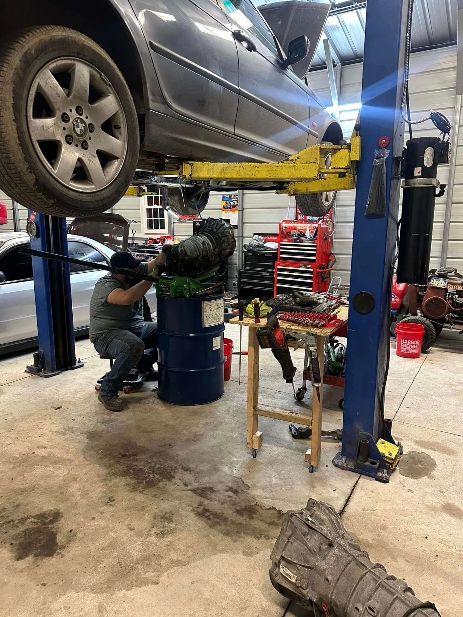 A man is working on a car on a lift in a garage.
