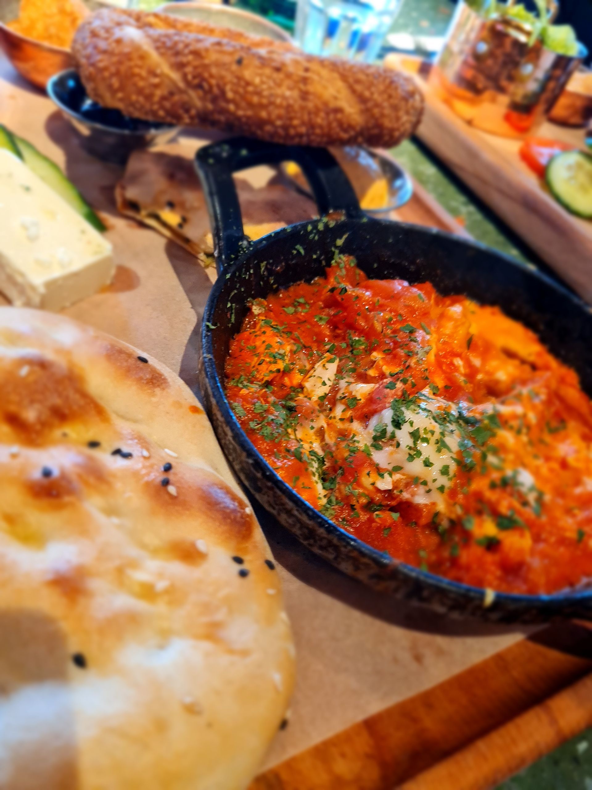 Nahaufnahme eines Brunch-Buffets mit Shakshuka in der Pfanne, Brot, Käse und anderen Beilagen.
