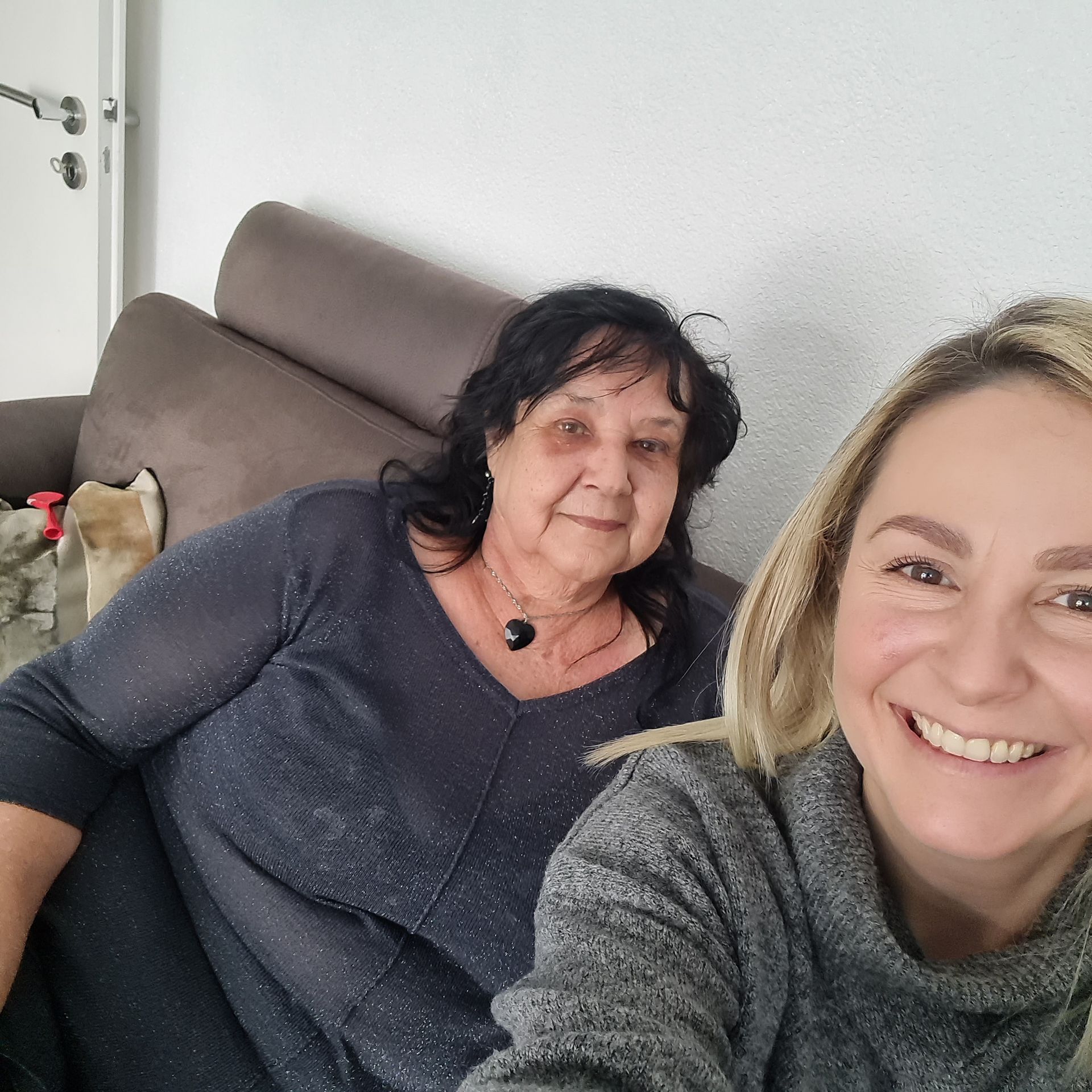 Zwei lächelnde Frauen sitzen auf einem Sofa. Die ältere Frau trägt ein graues Hemd. Die jüngere macht ein Selfie, die jüngere Frau ist Tamara .