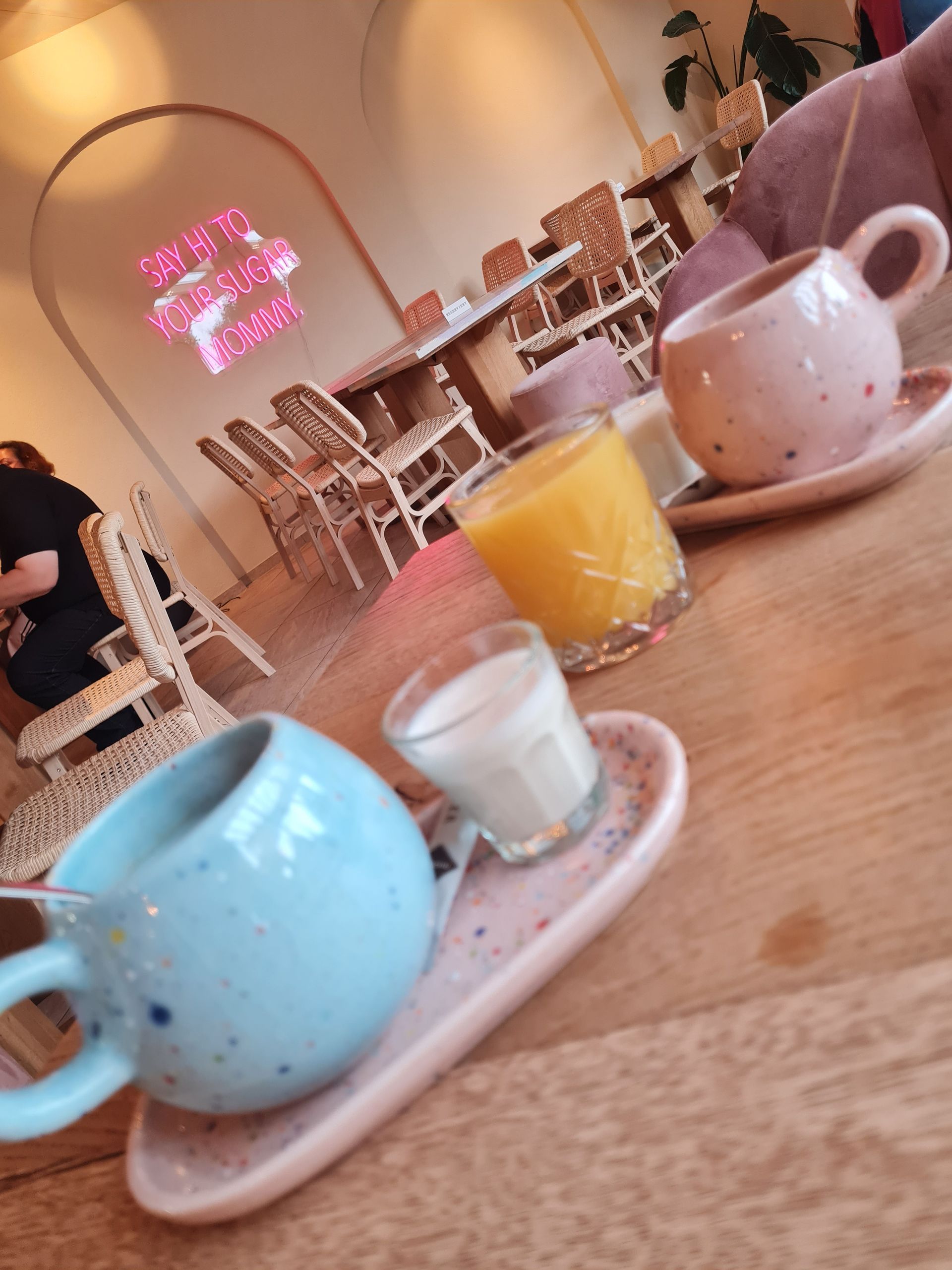 Tassen und Gläser mit Flüssigkeiten auf einem Holztisch in einem Café, hellblau und rosa. Brunch mit Kunden.
