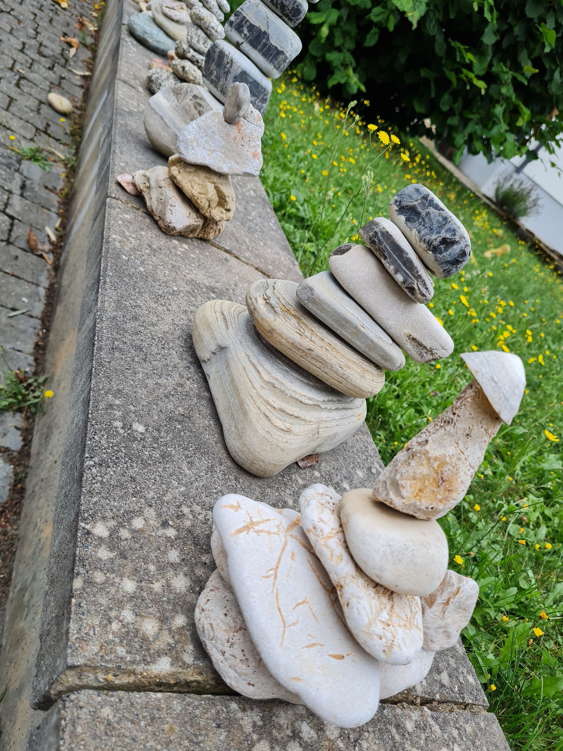 Im Freien sind auf einer Betonmauer gestapelte Steinhaufen zu sehen. Im Hintergrund sind Gras und weitere Steine ​​erkennbar.