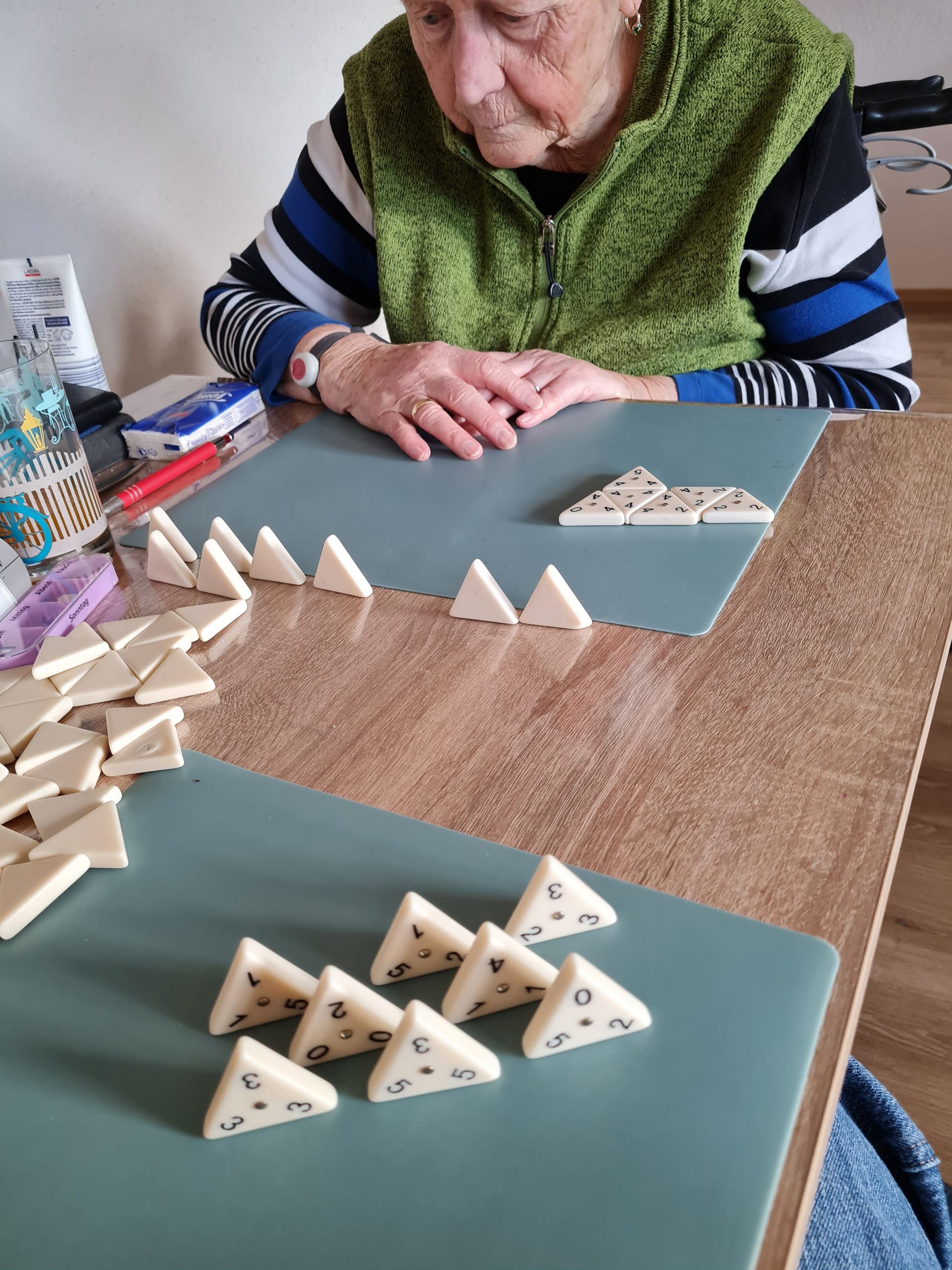 Eine ältere Frau spielt auf einem Tisch ein Dominospiel; die Spielsteine ​​liegen auf einer blauen Matte.