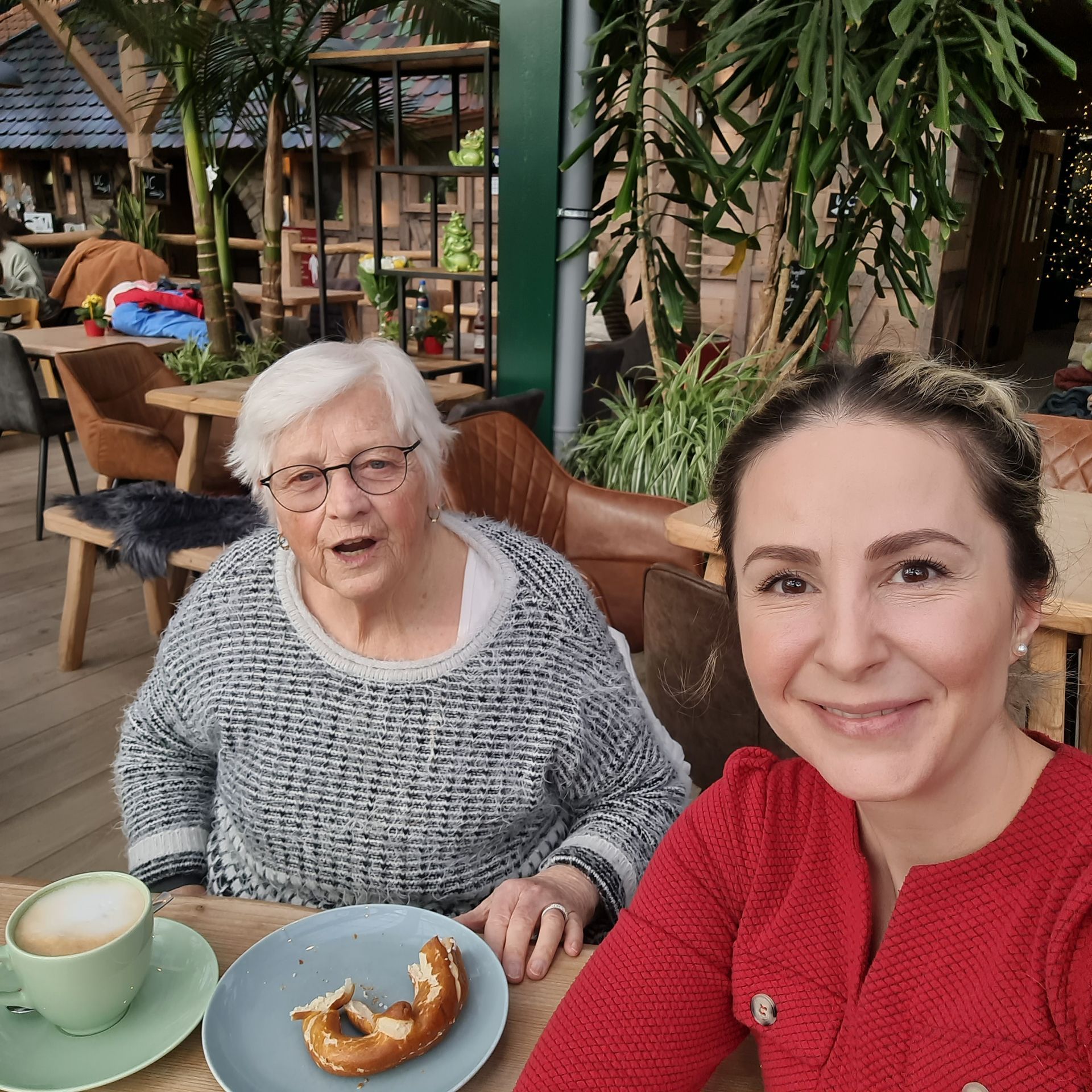 Eine Frau und eine ältere Person sitzen mit Speisen und Getränken an einem Tisch in einem Straßencafé.